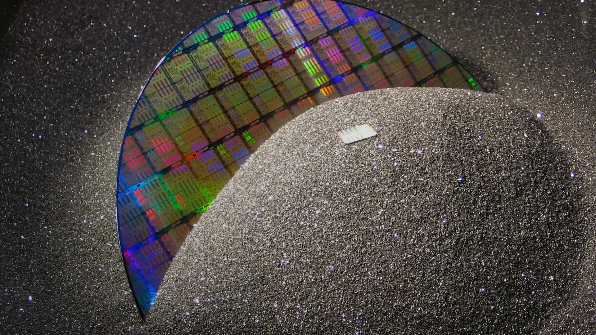 Close-up of a wafer reflecting a colorful spectrum of light against a dark speckled background.